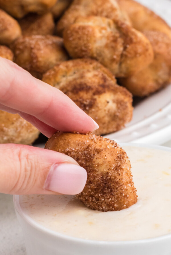 cinnamon sugar pretzel bites being dipped in a sugary glaze dipping sauce.