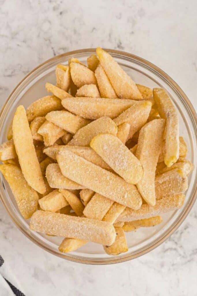 Frozen steak fries in a clear glass bowl on a marble table. 