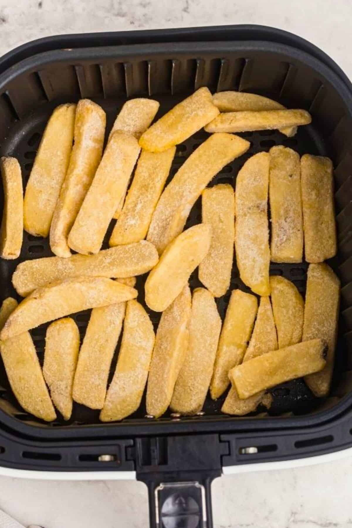 Frozen steak fries in the air fryer basket before being cooked. 