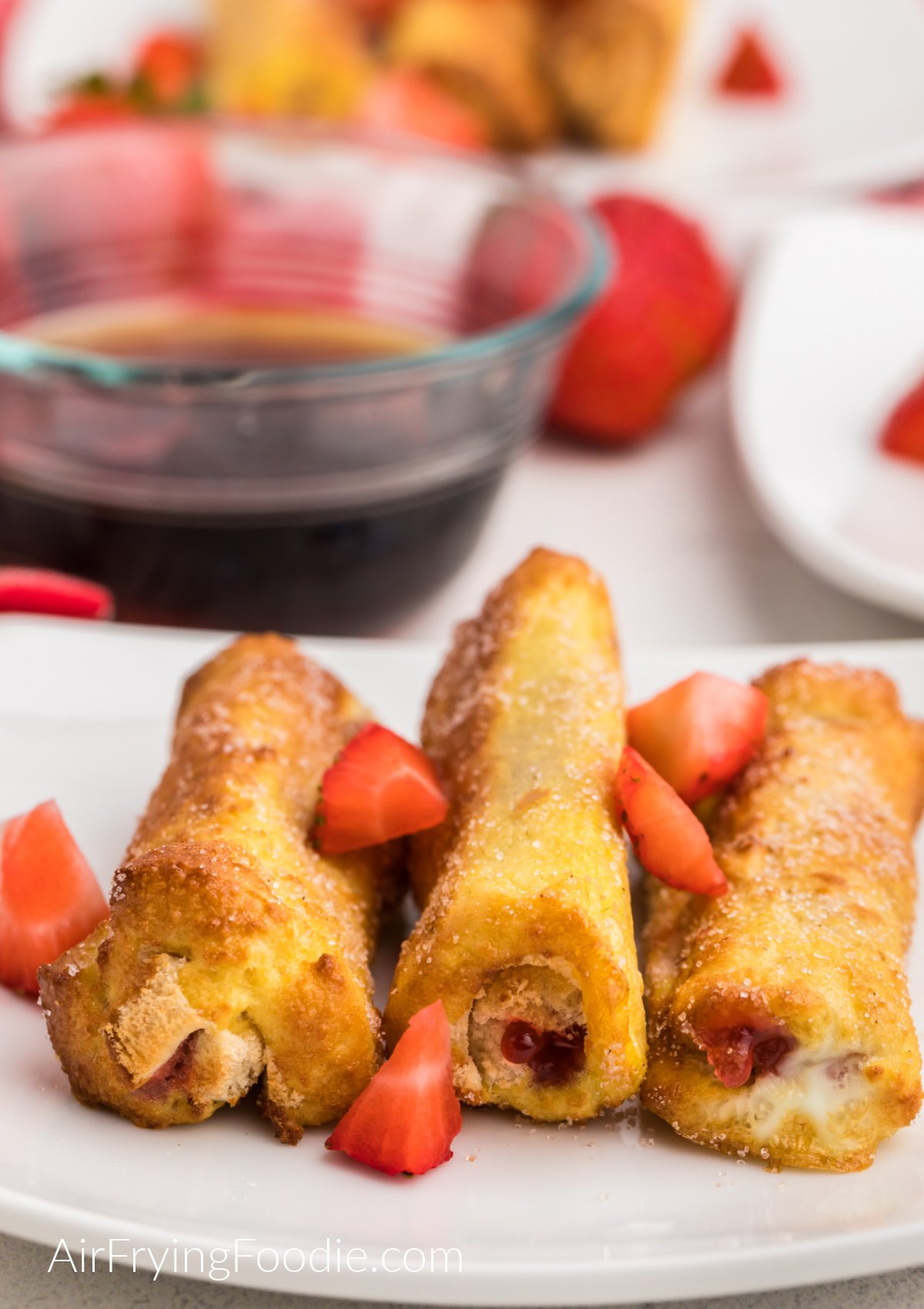Strawberry French Toast Roll Ups made in the air fryer on a white plate topped with fresh strawberries. 