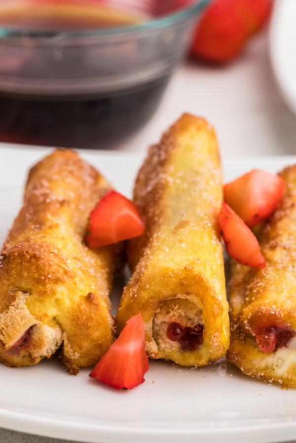 Air Fryer Strawberry french toast roll ups on a white plate and garnished with fresh cut strawberries.