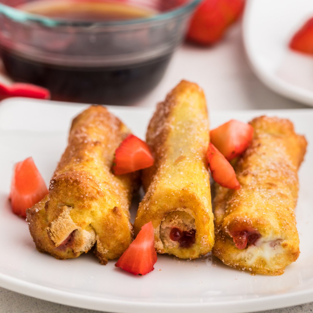 Air Fryer Strawberry french toast roll ups on a white plate and garnished with fresh cut strawberries.
