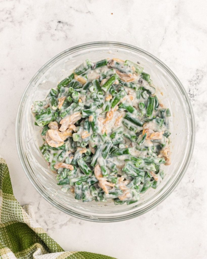 Bowl with mixed green beans and ingredients stirred together before cooking. 