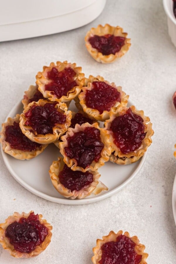 Cooked cranberry covered brie bites in phyllo shells in front of an air fryer and served on a white plate.