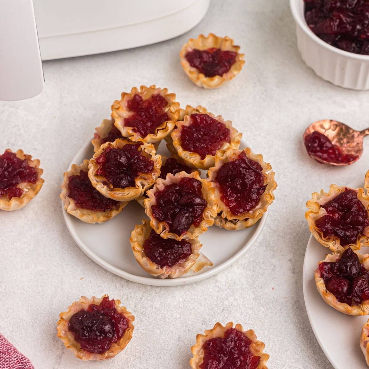 Cooked cranberry covered brie bites in phyllo shells in front of an air fryer and served on a white plate.