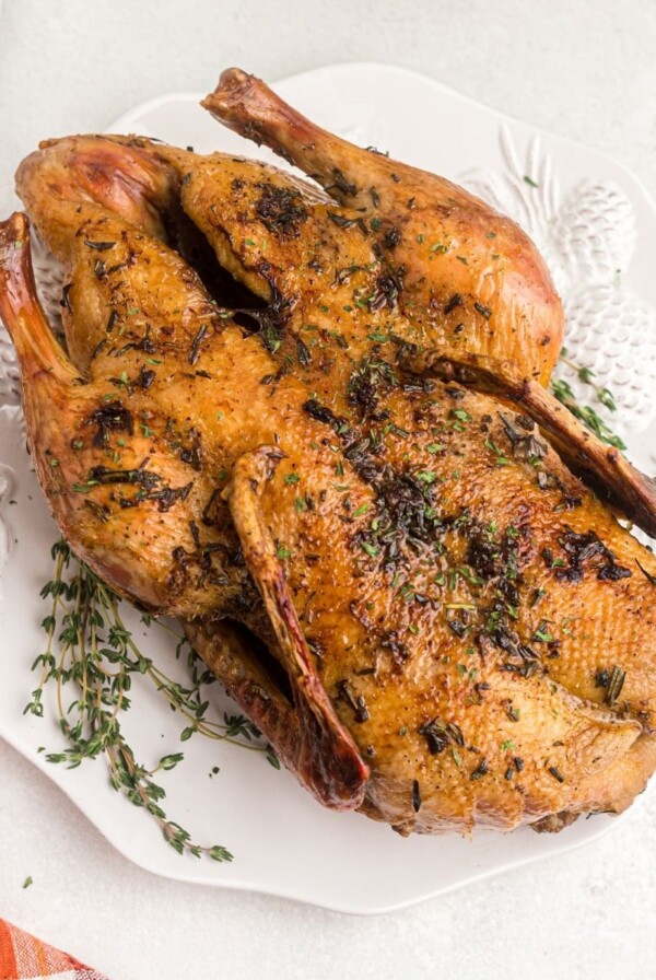 Whole golden duck on a white platter with a sprig of thyme