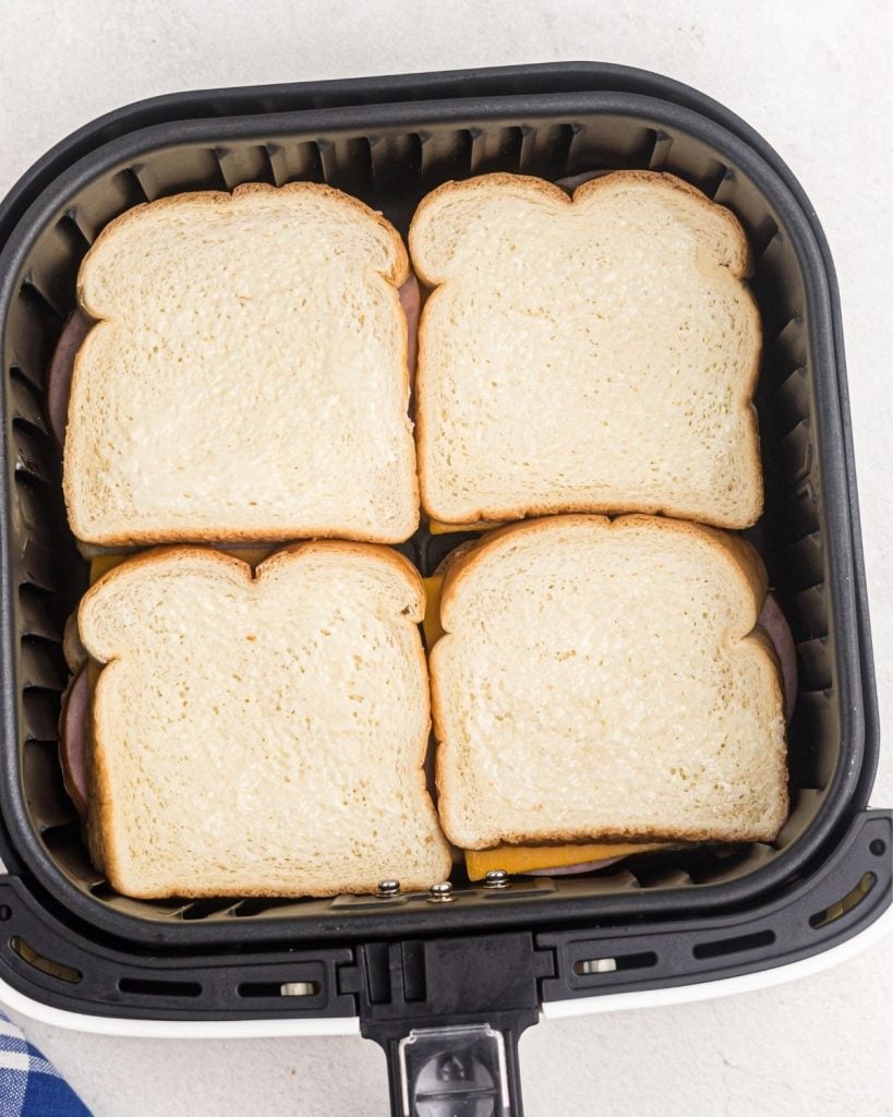 Four butter ham and cheese sandwiches in an air fryer basket before being cooked. 