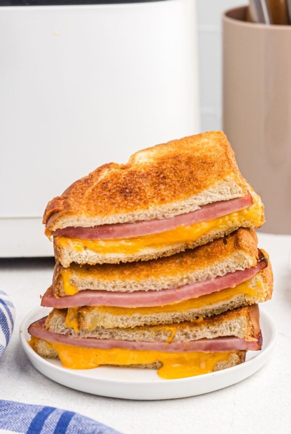 Close up photo of ham and cheese sandwiches, golden and with melted cheese dripping out onto plate.