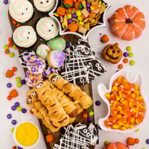 Overhead of board filled with brownies, cupcakes, mummy dogs, donut holes and candy scattered around the table.