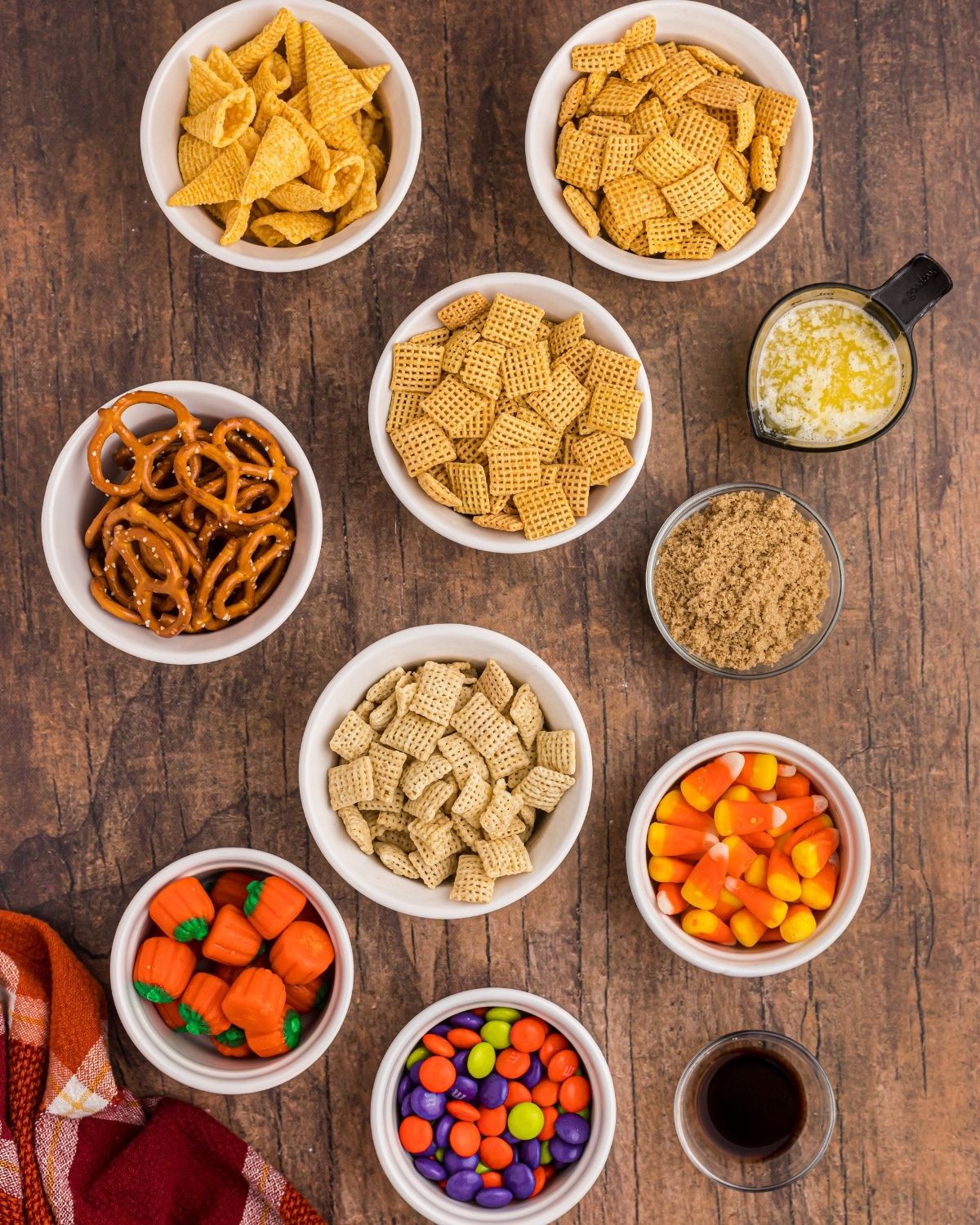 Spooky Air Fryer Halloween Chex Mix 4 Ingredients in small bowls on a wooden table. Cereals, melted butter, brown sugar, candies, and vanilla.