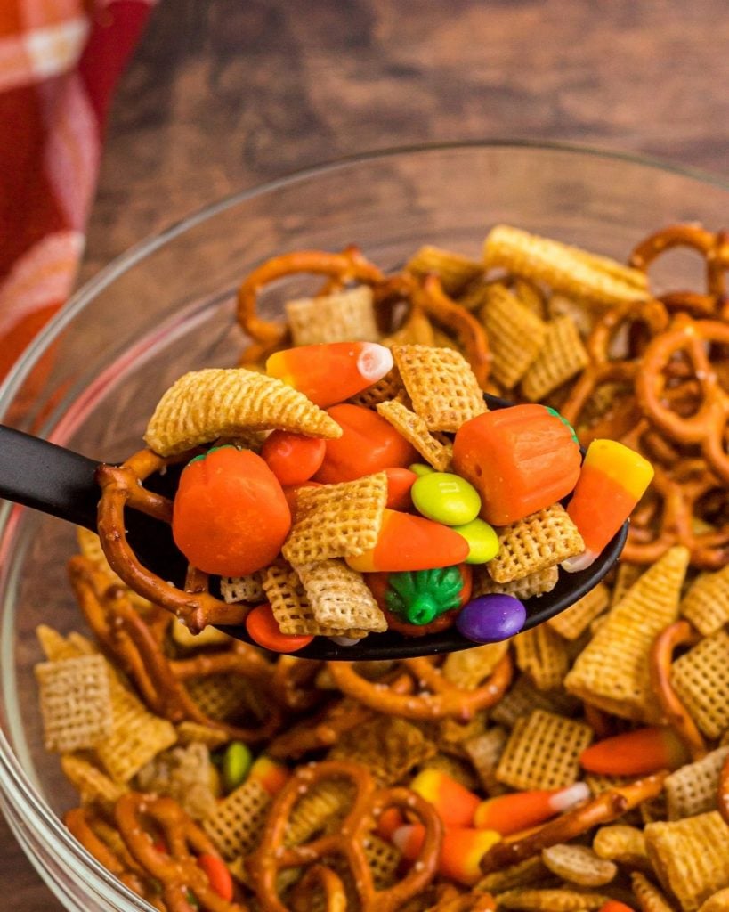 Close up of spoon filled with Chex mix cereals, and Halloween candies.
