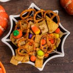 Spider web shaped black bowl filled with chex mix, Halloween candies, and pretzels.