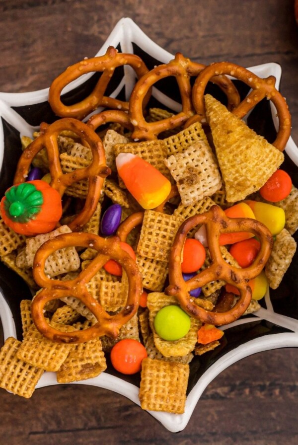 Spider web shaped black bowl filled with chex mix, Halloween candies, and pretzels.