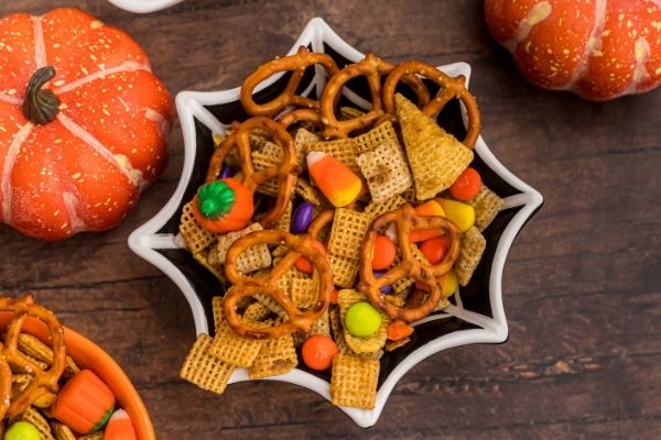 Picture of black spider web ceramic bowl filled with Halloween candies, Chex cereal and pretzels. 