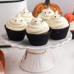 Chocolate cupcakes on a white cake stand with ghost vanilla frosting and candy eyes.