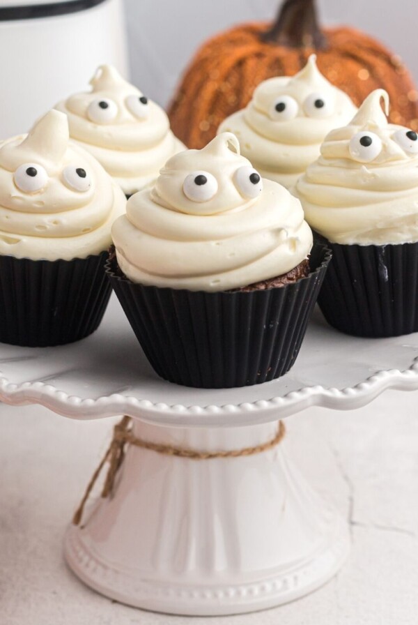 Chocolate cupcakes on a white cake stand with ghost vanilla frosting and candy eyes.