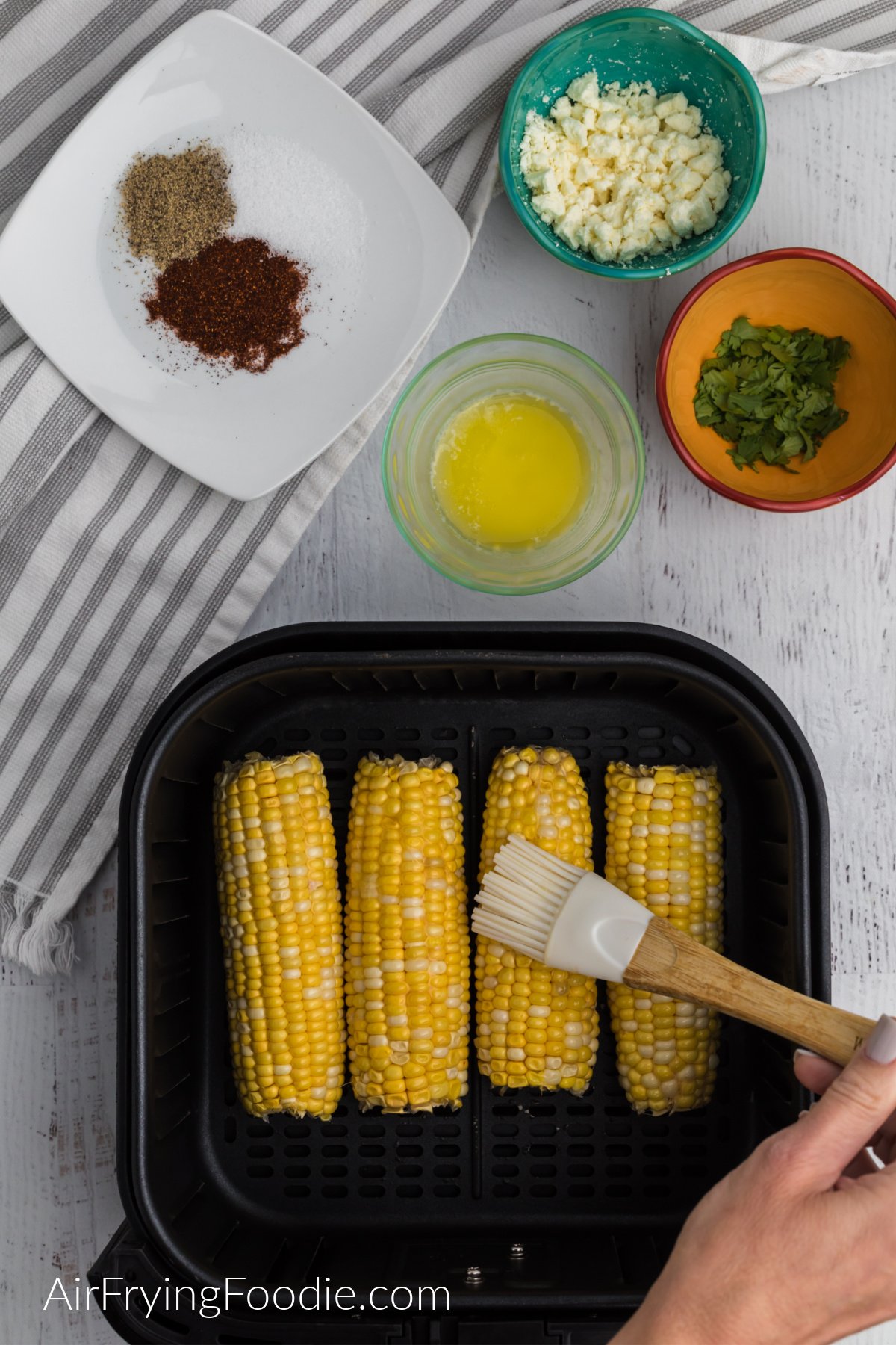 Brushing butter onto the corn in the air fryer basket.