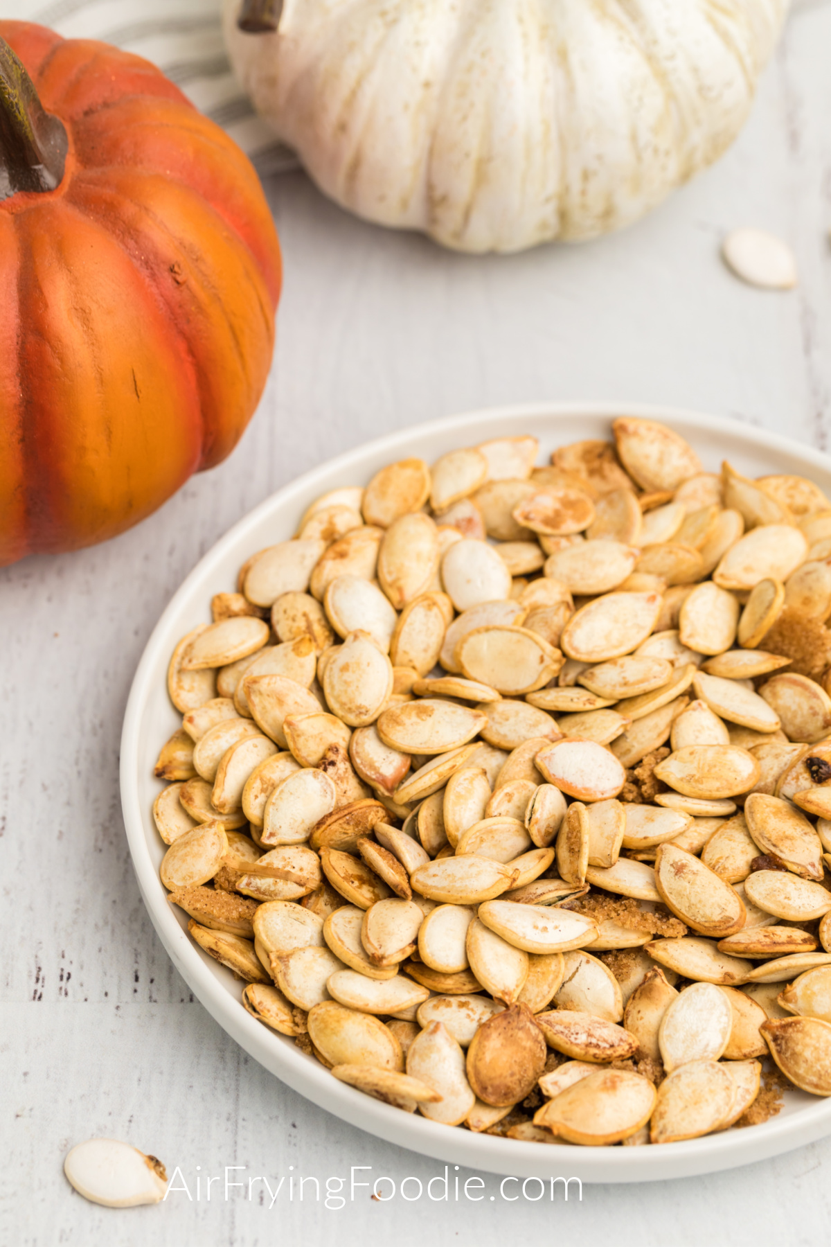 Pumpkin seeds made in the air fryer and served on a white plate with pumpkins surrounding them.
