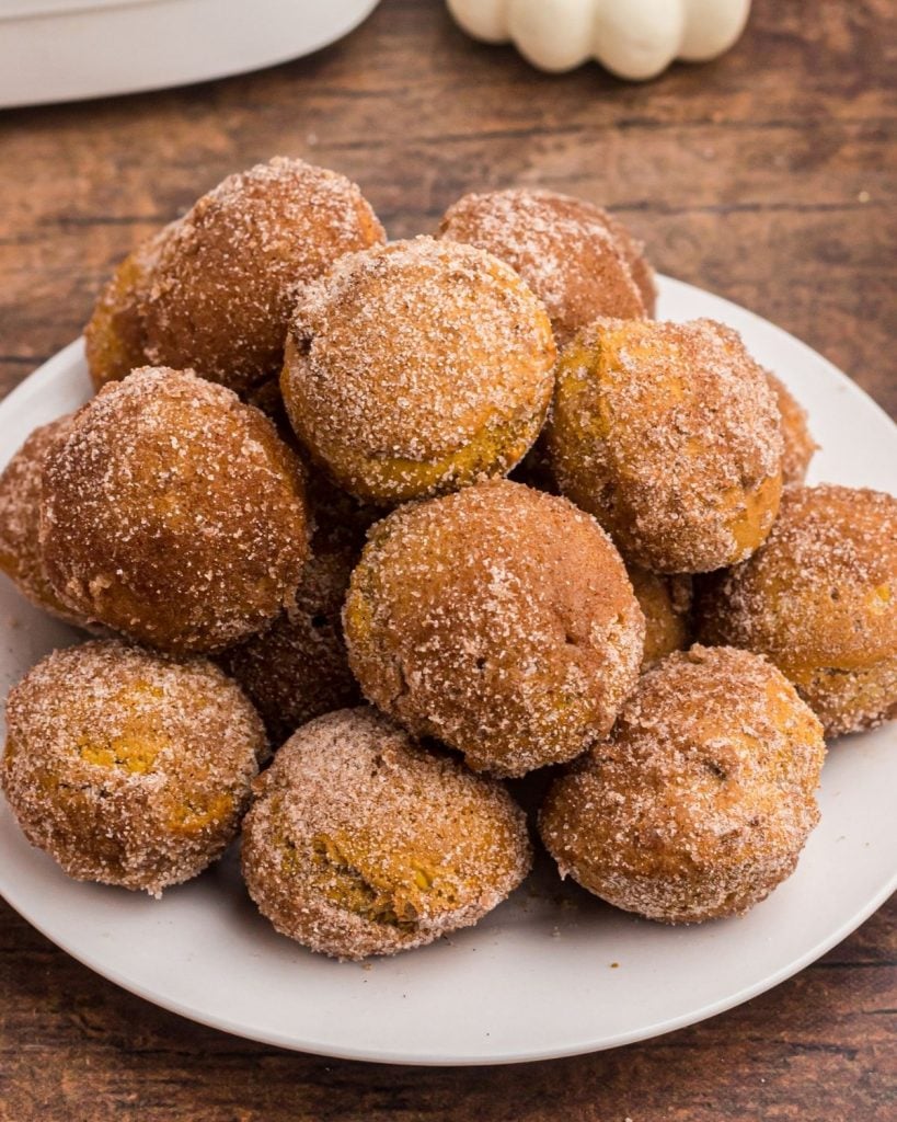 Close up photo of golden and sugar coated donut holes, on a white plate. 