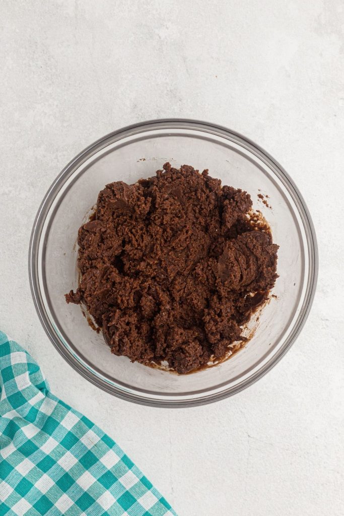 Ingredients stirred together to a thick fudgy brownie batter in a clear glass bowl. 