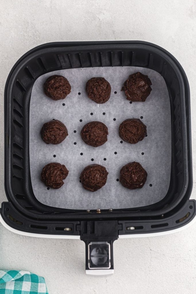 Nine scoops of cookie batter in the air fryer basket on parchment paper before being cooked
