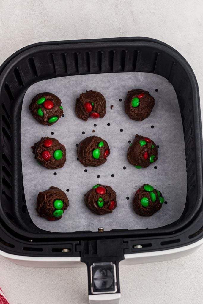 Scooped balls of brownie cookie mix dough in the air fryer basket before being cooked. 