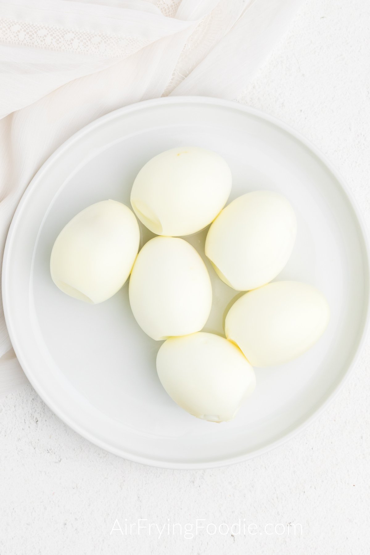 Boiled and peeled eggs that were made in the air fryer - on a white plate.