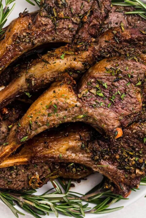 Golden brown and juicy lamb chops stacked on a white plate.