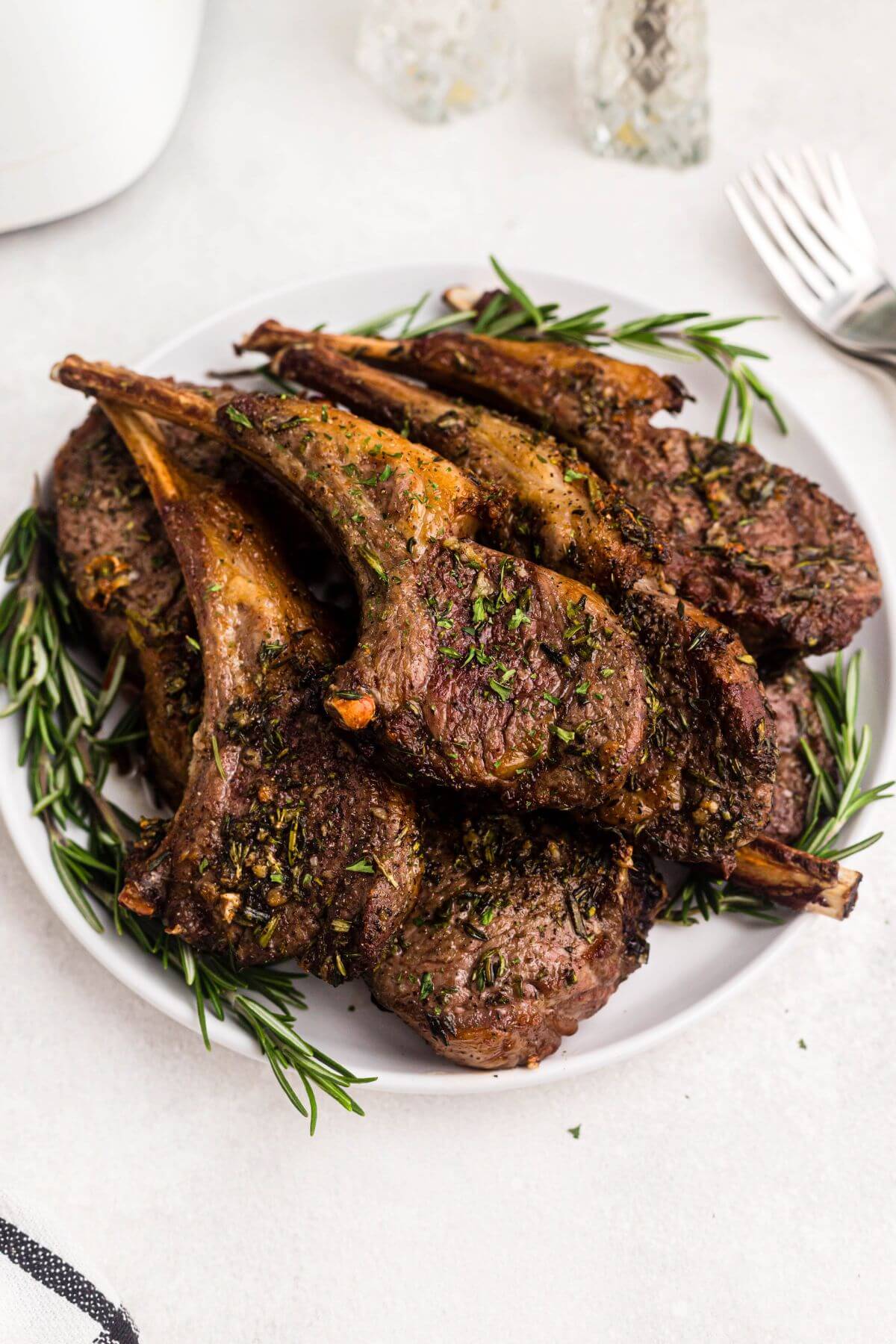 Brown and juicy lamb chops stacked on a white plate garnished