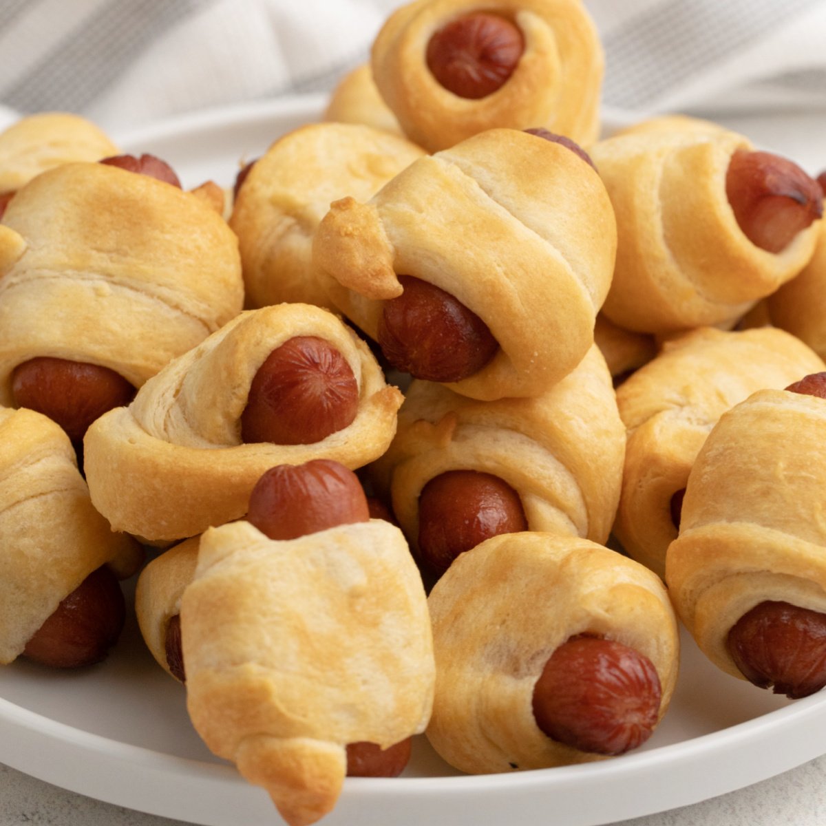 Close up photo of air fryer pigs in a blanket on a white plate ready to be served.