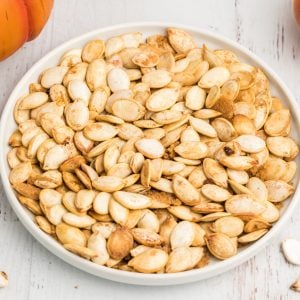 Roasted air fryer pumpkin seeds on a white plate sprinkled with cinnamon, salt, and brown sugar.