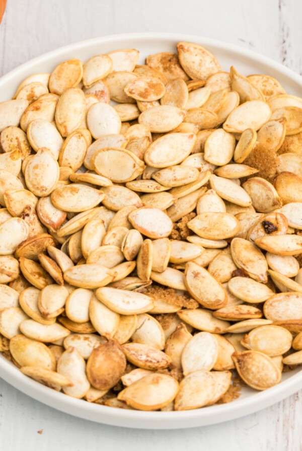 Roasted air fryer pumpkin seeds on a white plate sprinkled with cinnamon, salt, and brown sugar.