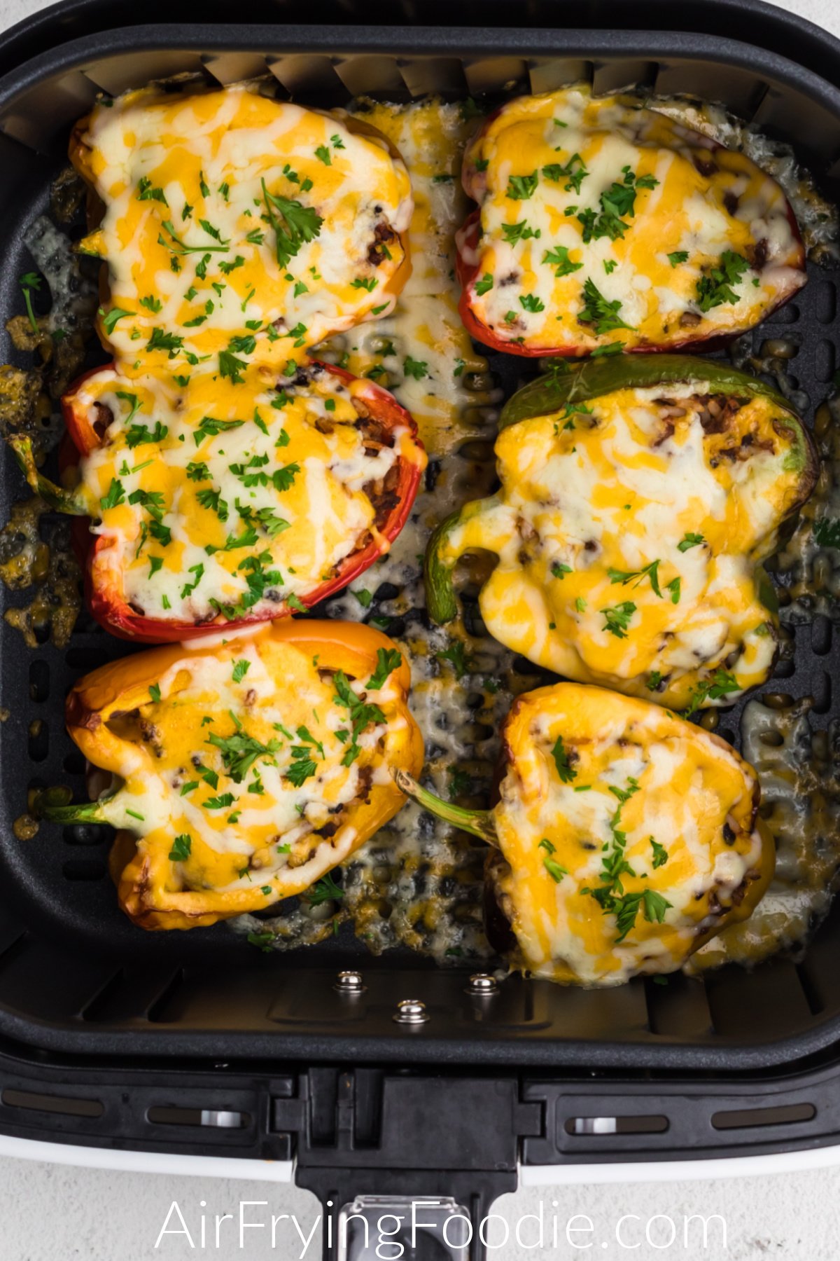 Stuffed peppers topped with cheese and fresh parsley in the basket of the air fryer. 