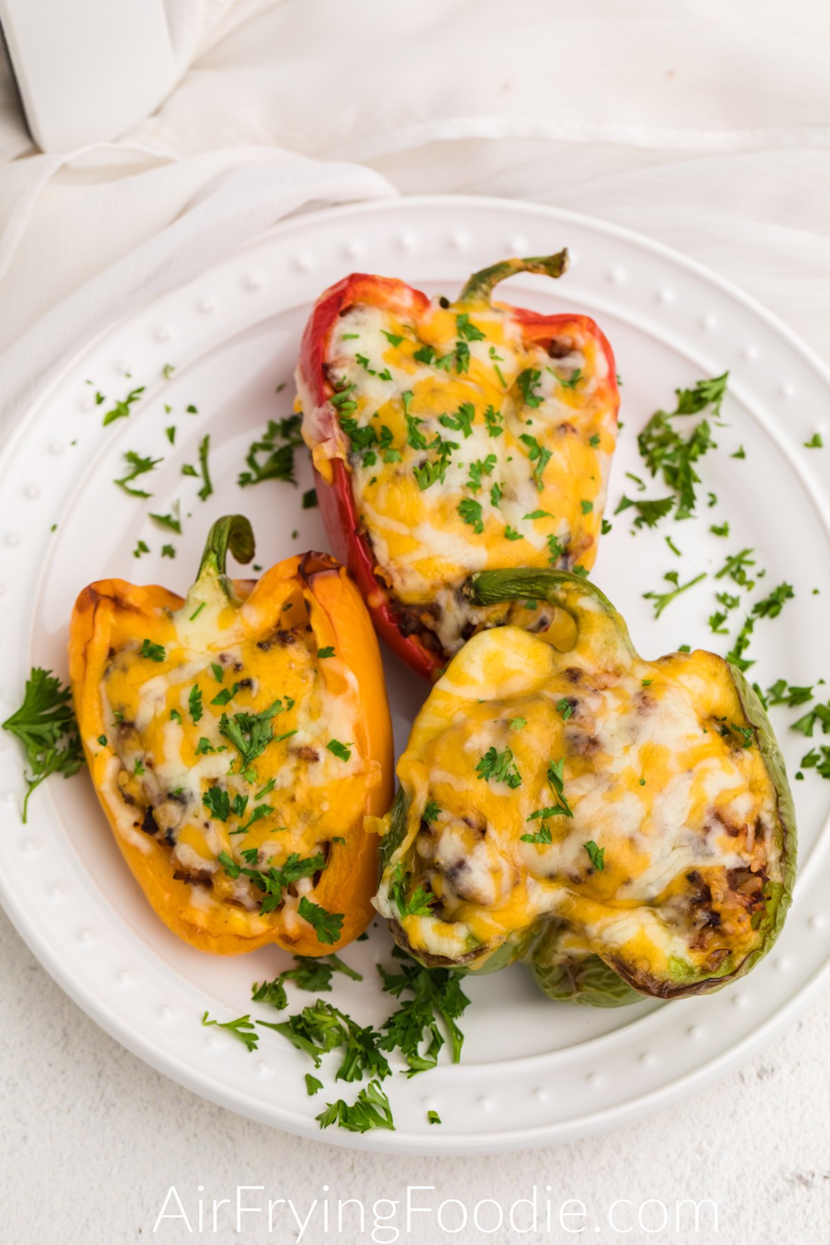 Air Fryer Stuffed Peppers on a white plate garnished with cheese and fresh parsley.
