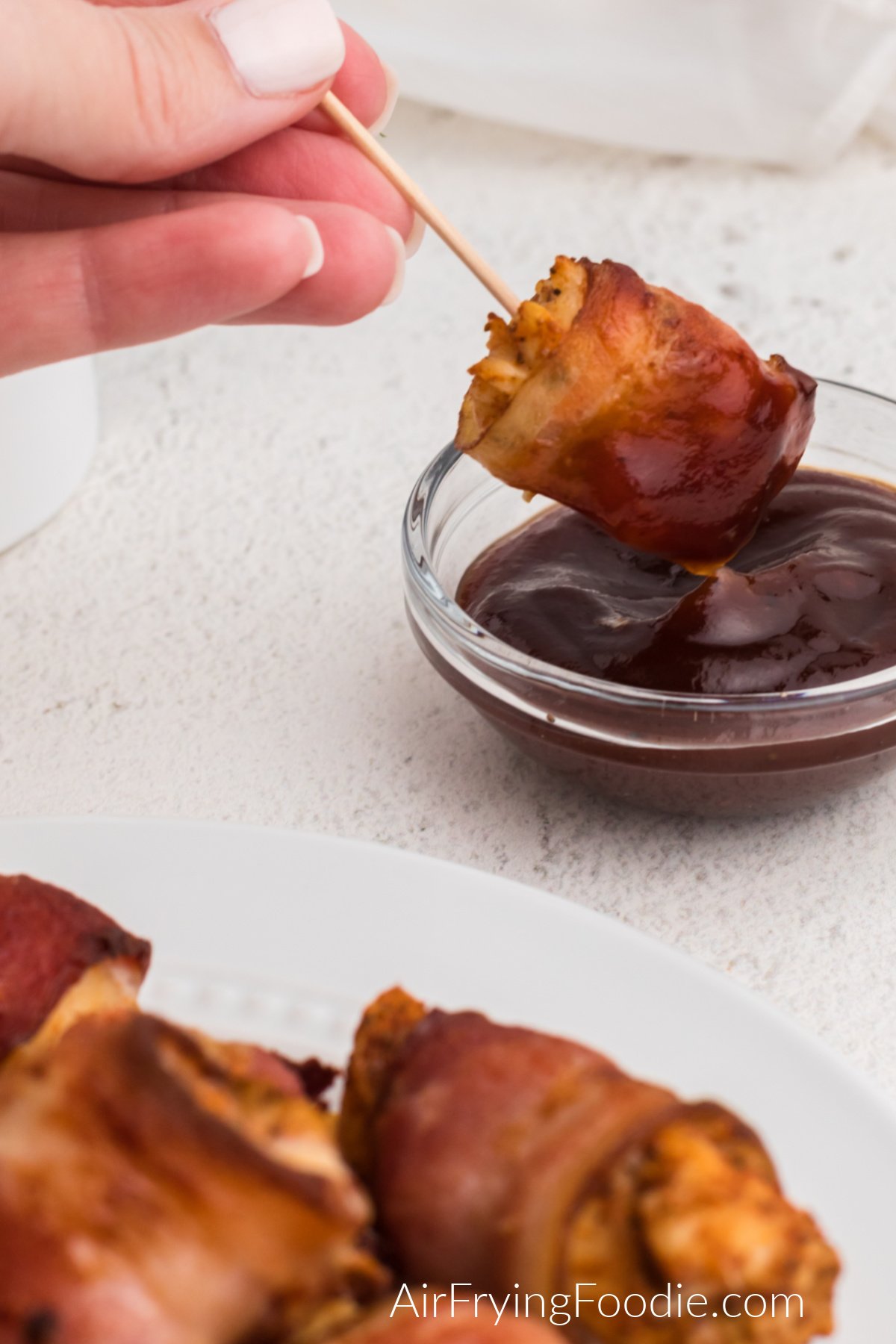 Bacon wrapped chicken bites being dipped in BBQ sauce. 