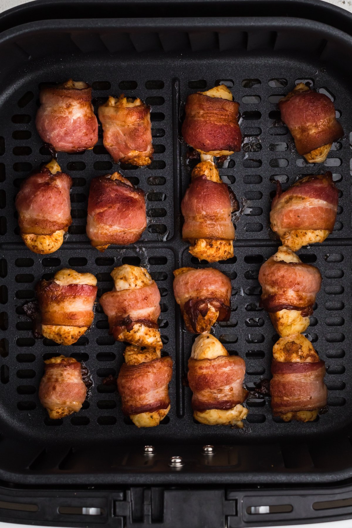 Fully cooked bacon wrapped chicken bites in the basket of the air fryer. 