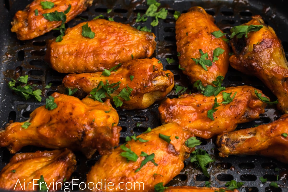 chicken wings in air fryer basket tossed in sauce and garnished with fresh parsley.