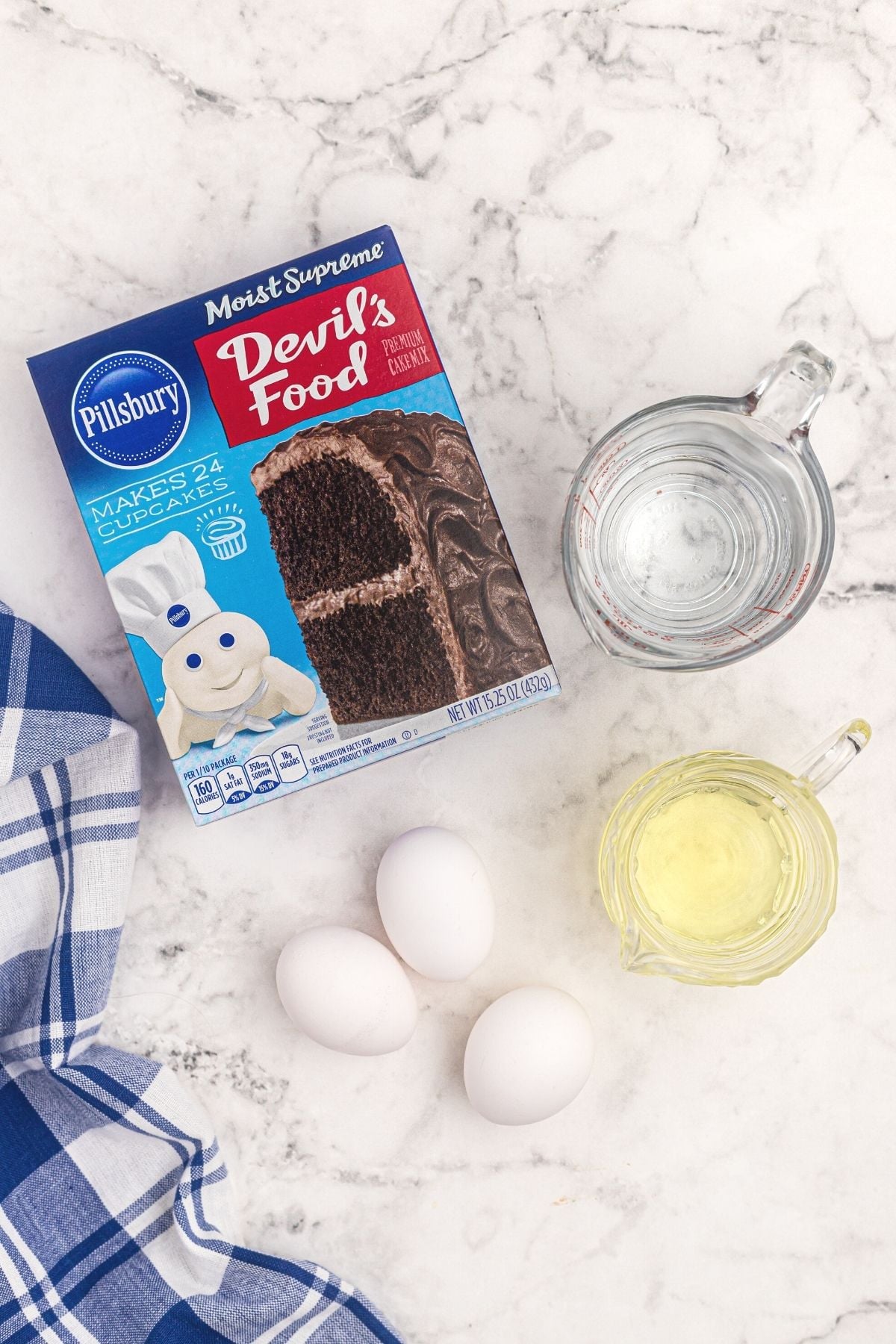 Box cake mix with oil, eggs, and water needed to make cake in air fryer on a white marble board
