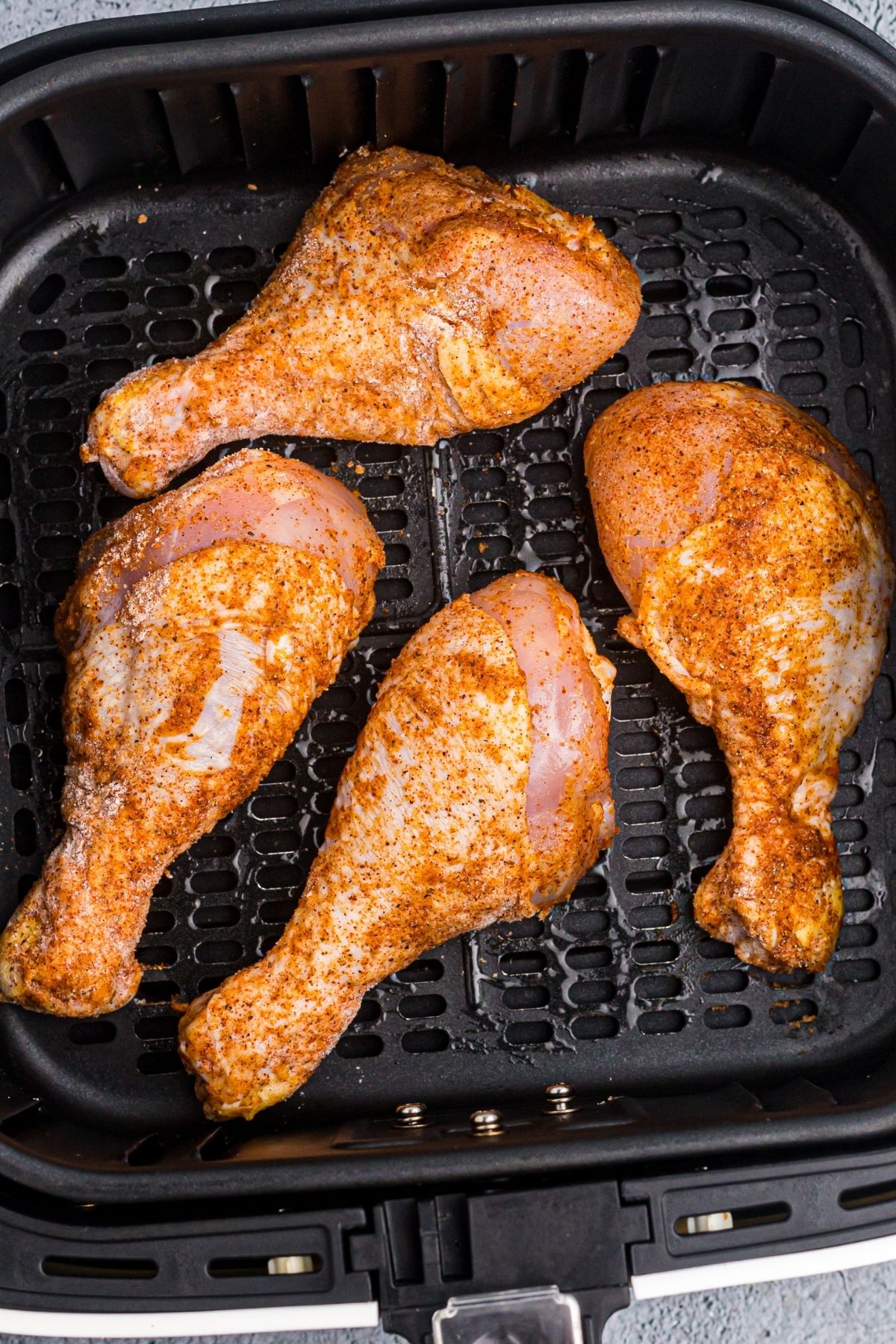Seasoned chicken drumsticks in the air fryer basket before being cooked. 
