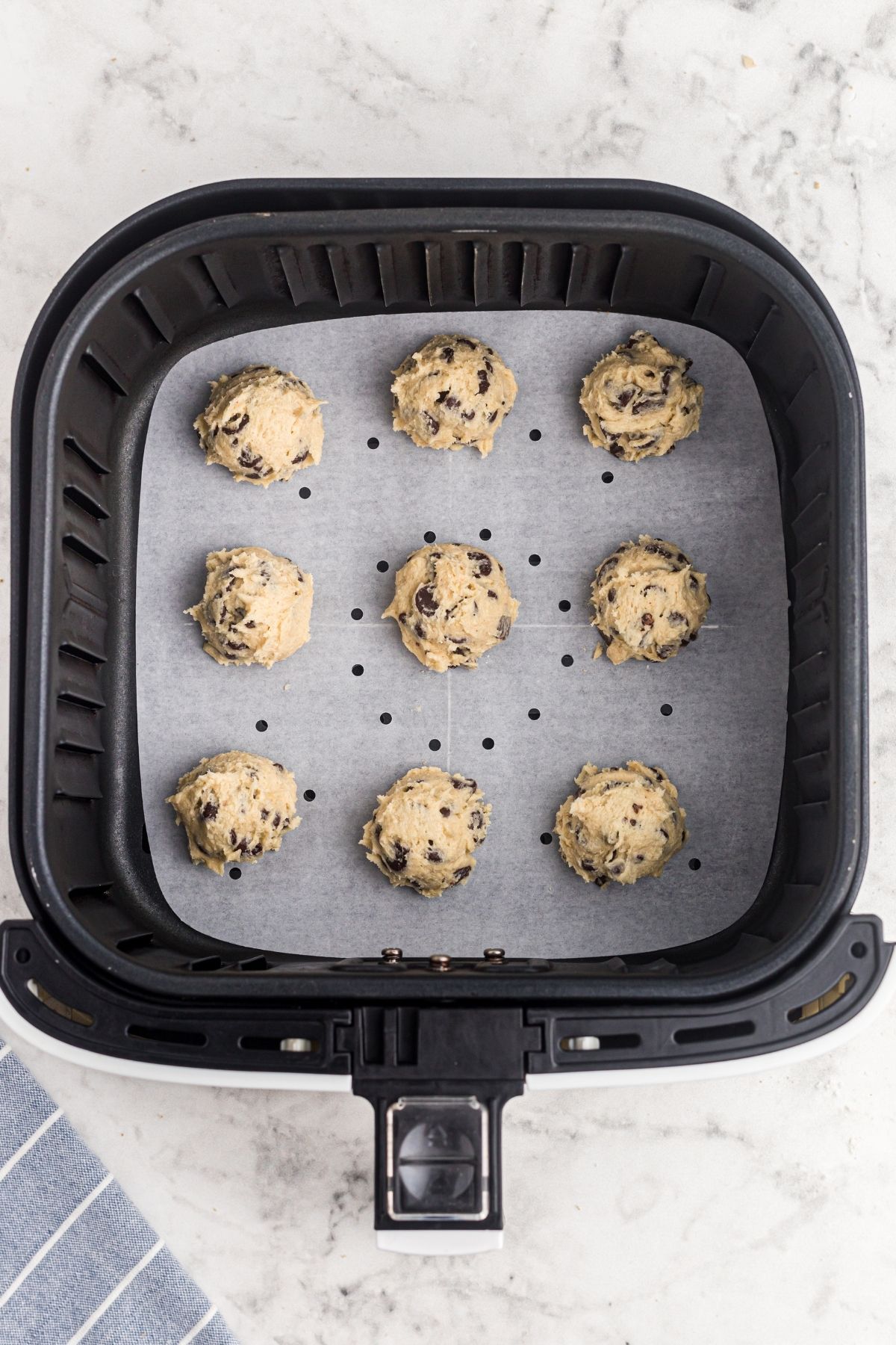 Balls of cookie dough in the air fryer basket lined with parchment paper