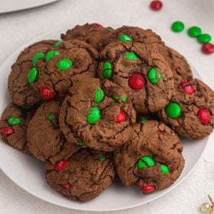 Freshly baked chocolate brownie cookies with red and green m and m's baked in.. Served on a white plate.