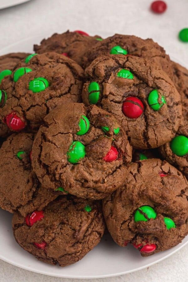 Freshly baked chocolate brownie cookies with red and green m and m's baked in.. Served on a white plate.