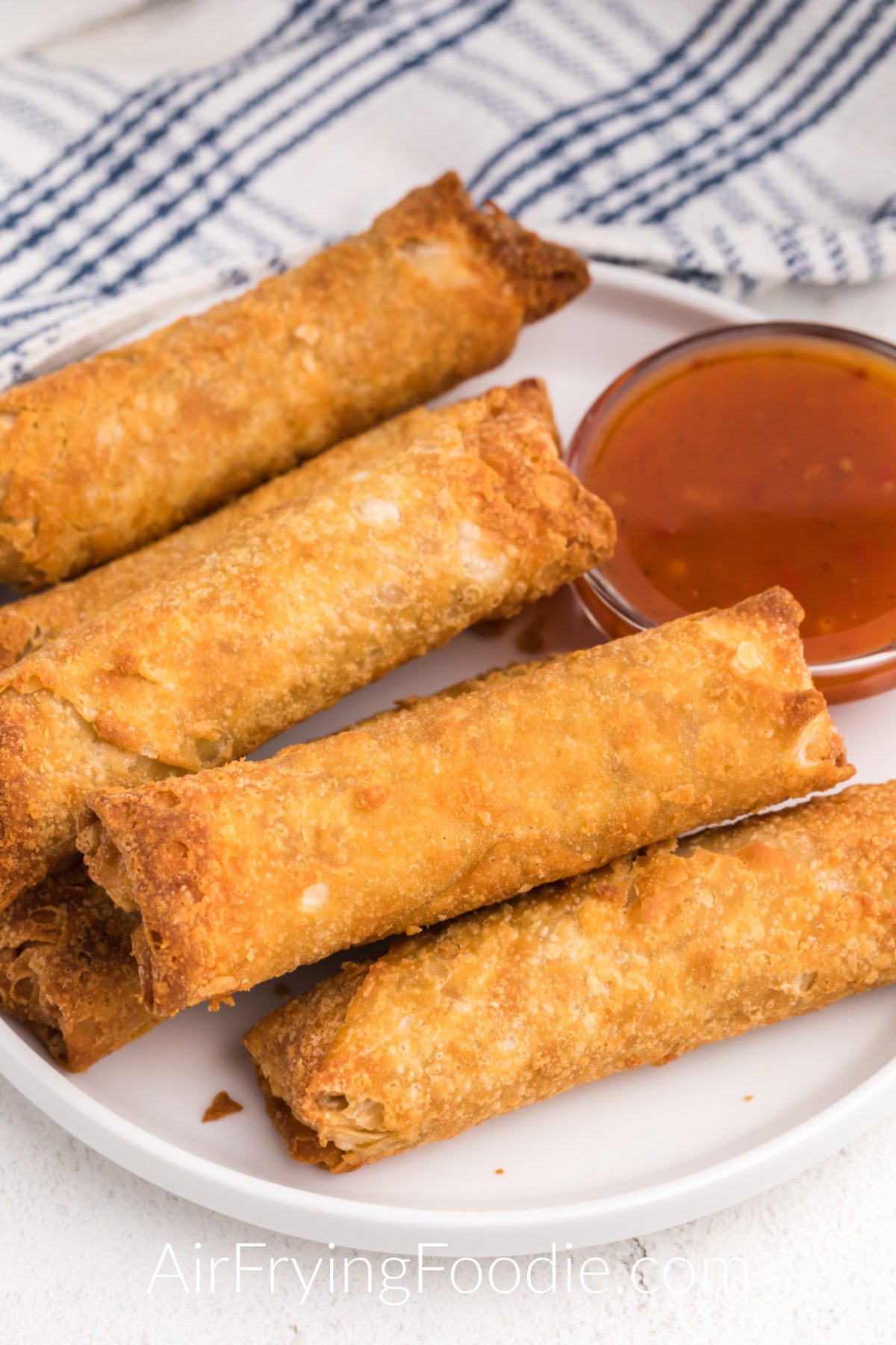 Crispy cooked golden brown frozen egg rolls made in the air fryer served on a white plate with dipping sauce.