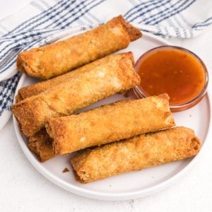 Egg rolls on a white plate with a side of dipping sauce.