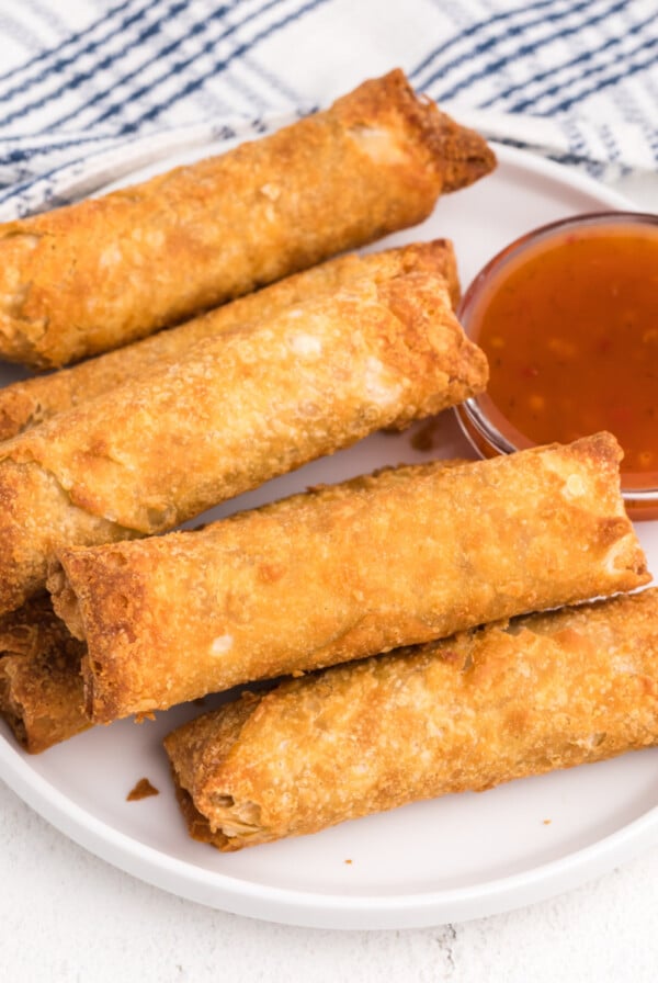 Egg rolls on a white plate with a side of dipping sauce.