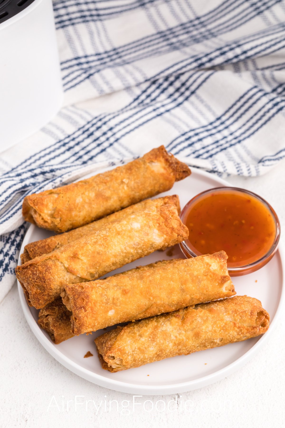 Frozen egg rolls that have been fully cooked in the air fryer. Served on a white plate with Thai chili sauce.
