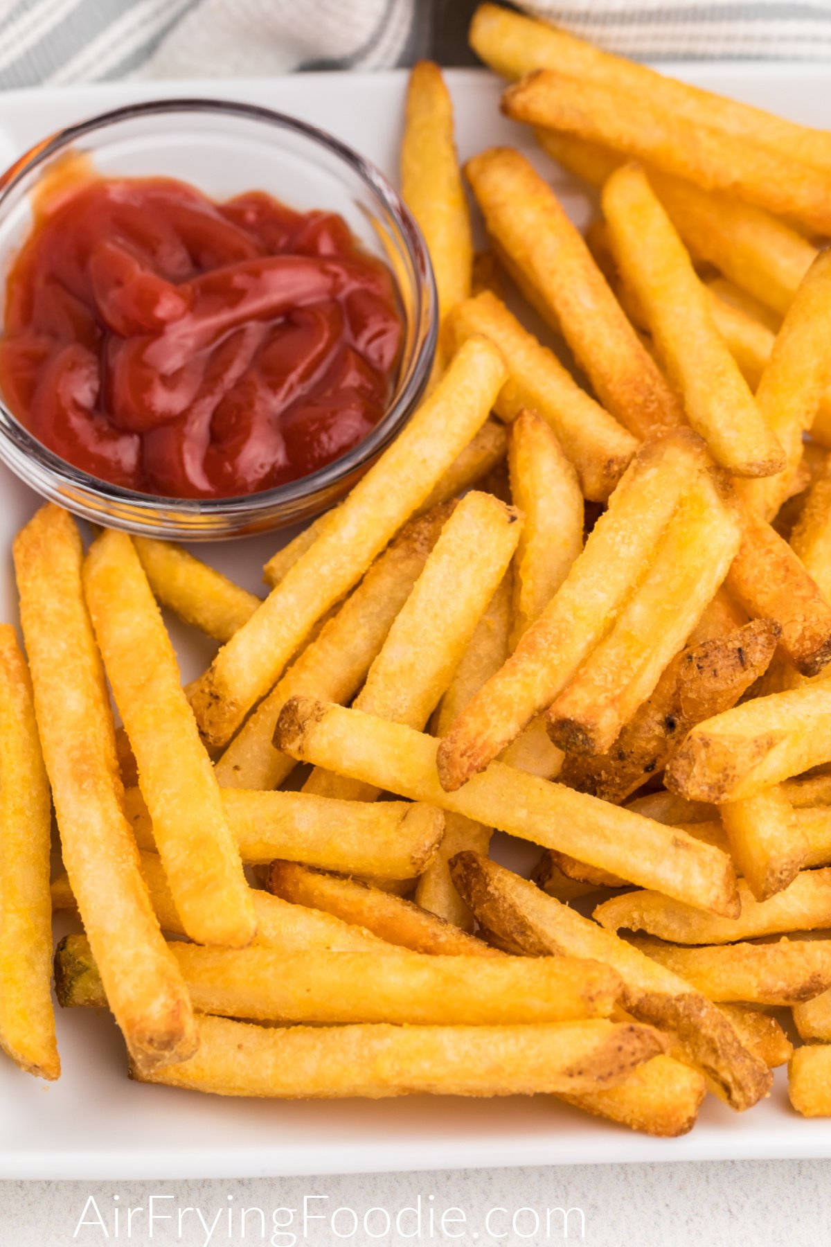 Close up of french fries that were cooked from frozen in the air fryer on a white plate with a side of ketchup.