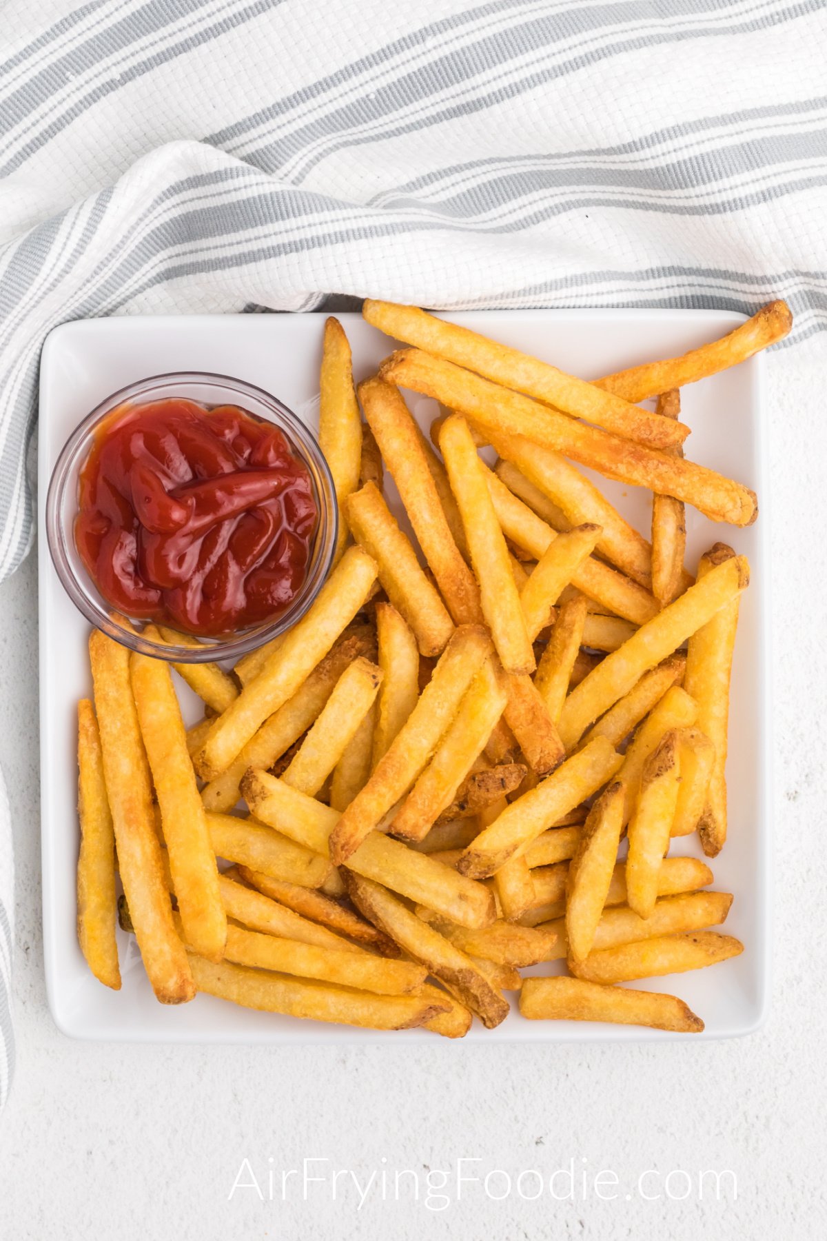 French fries made in the air fryer from frozen, served on a white plate with a side of ketchup.