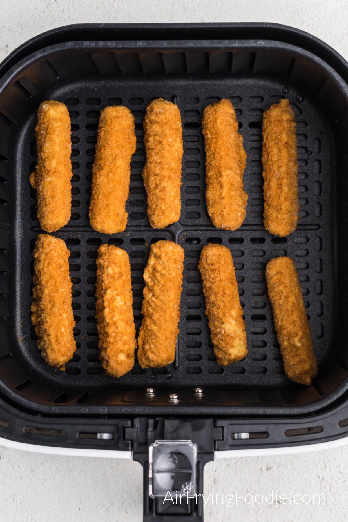 Frozen mozzarella sticks placed in a single layer in the air fryer basket ready to cook.