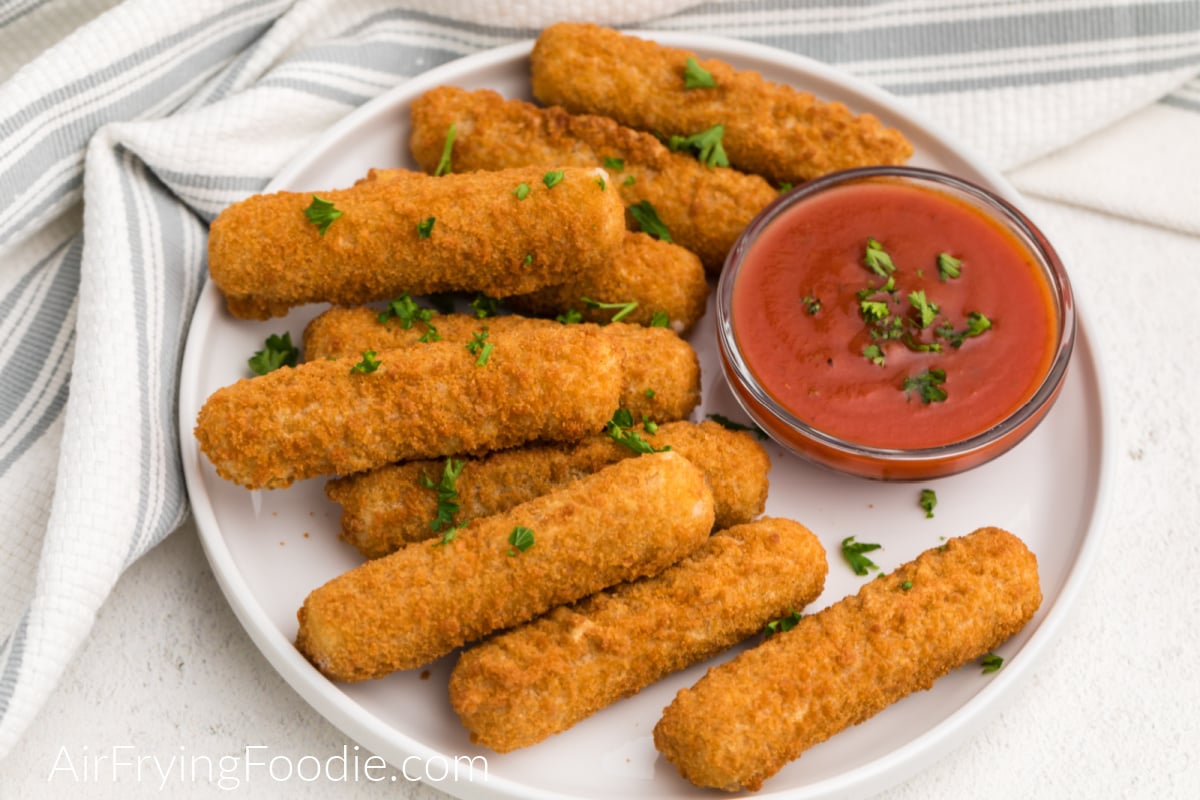 Mozzarella cheese sticks that were frozen and then air fried - placed on a white plate and topped with fresh parsley. 